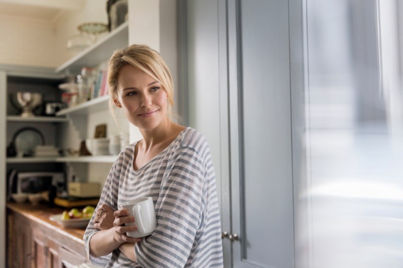 En kvinne står med kaffekoppen i hånden på kjøkkenet
