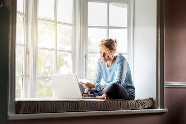 En dame sitter i en vinduskarm og kikker på en laptop